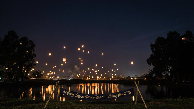 Yi peng sky lantern festival in chiang mai, thailand, with glowing lanterns floating in the night sky above a reflective lake