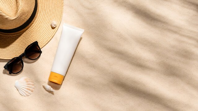 Sunscreen, Sunglasses and Straw Hat on Sandy Beach