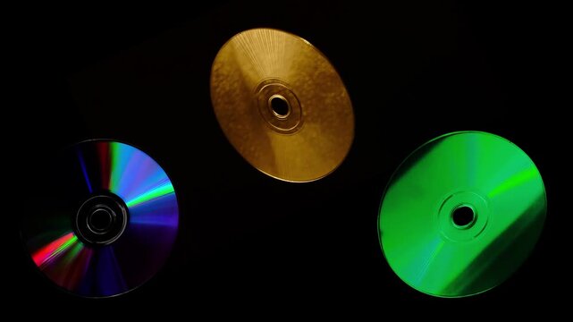 Rainbow light reflecting of a surface of a rotating CD-DVD disk against a dark background, highlight their reflective surfaces in different ways