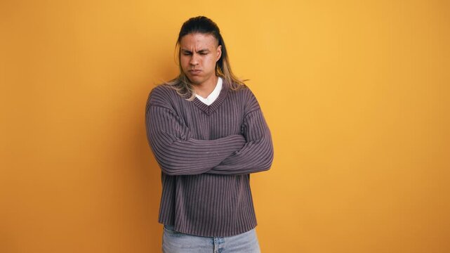 Displeased young man with long hair standing with his arms crossed. He is frowning and shaking his head in a gesture of disagreement