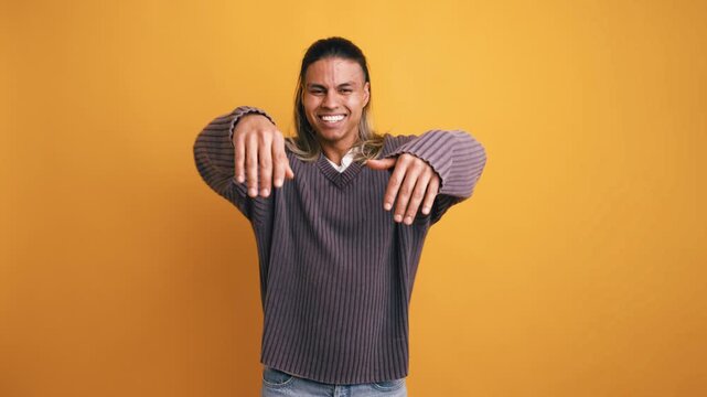 Young energetic latino man dancing and having fun. Expressive male model with long hair moving to the music against a vibrant yellow background