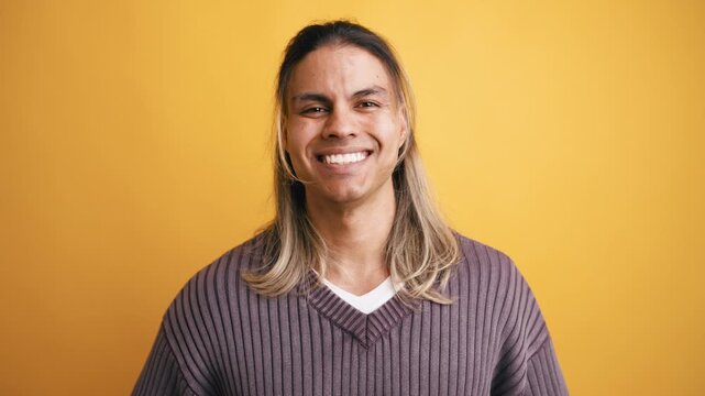 Charming young latino man with long hair looking at the camera with a joyful and friendly smile. Portrait of a happy person in a studio