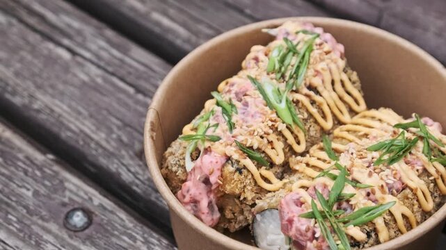 Slow pan showcases crispy tempura sushi rolls drizzled with creamy sauces and green onions. The vibrant colors and textures emphasize a delicious modern fusion street food.