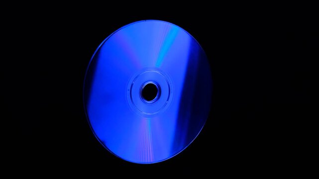 Rainbow light reflecting of a surface of a rotating CD-DVD disk against a dark background, highlight their reflective surfaces in different ways
