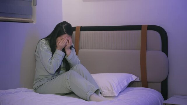 Stressed woman sits on bed anxiety depression or mental disorder crying sadly in pajamas with hands covering face, looking distressed in dark bedroom. Night bedtime. Expression shows emotional pain