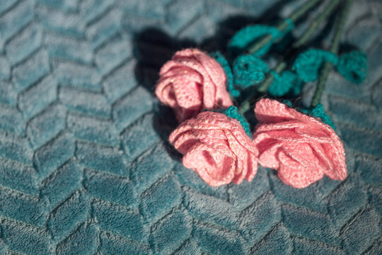 Knitted pink roses arranged on green fabric, craft still life