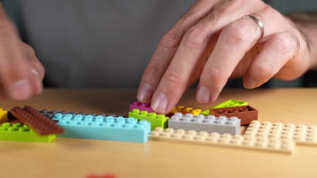 Creative man with building and assembling colorful toy blocks on a wooden table, enjoying a relaxing hobby that recalls childhood memories and stimulates creativity