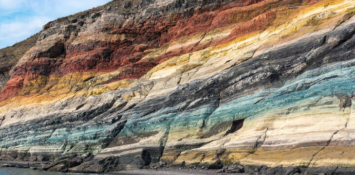 Close-up of a rugged mountain cliff showing distinct multi-colored sedimentary rock layers with sedimentary colorful geological landscape formation mountain background cliffside