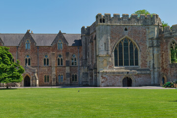 Fototapeta premium A grand stone building, likely a historic palace or castle, stands under a clear blue sky, fronted by a lush green lawn - The Bishop's Palace & Gardens - Wells - Somerset - UK