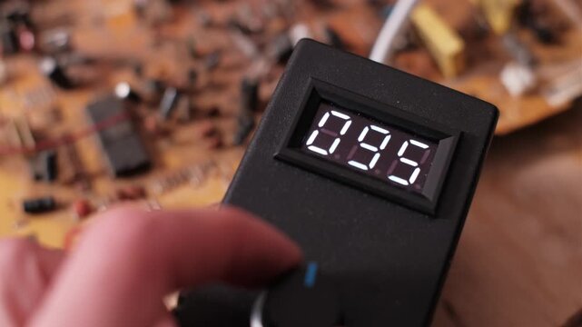 Close-up view of a hand turning a control knob to increase the numbers on a digital display. The adjustment signifies changing electrical parameters and testing device output.