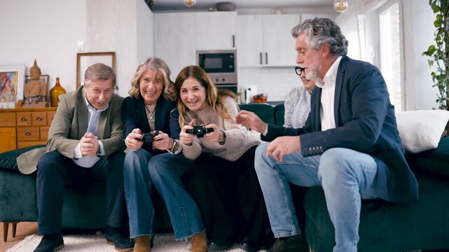 Happy senior friends sitting on the sofa, laughing and cheering while playing video games together. Modern group of mature people having fun