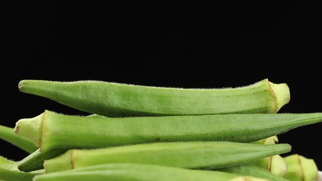 Pile of fresh raw okra pods slowly rotating on a black background.