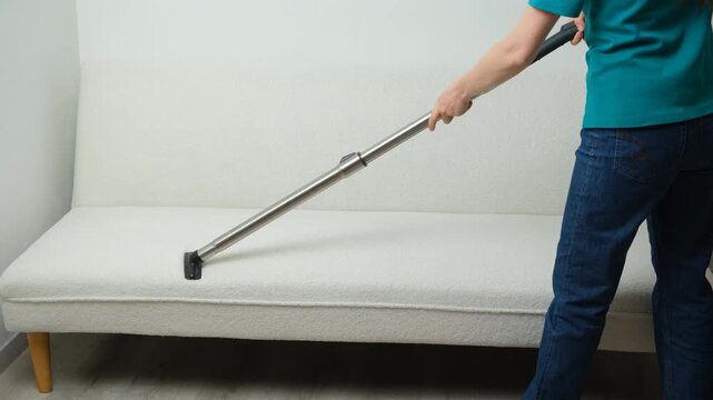 Woman cleaning white sofa with vacuum cleaner nozzle close up.
