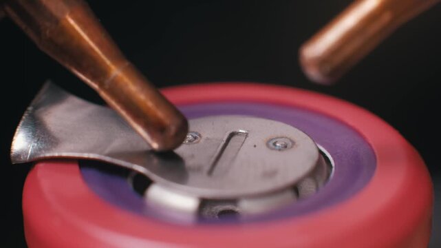 Extreme macro view of copper probes spot welding a nickel connector to a lithium battery terminal. The detailed industrial texture highlights precision engineering and manufacturing.