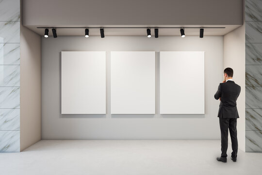 Business person thoughtfully viewing three large blank vertical canvases in a bright modern gallery exhibition under spotlights.