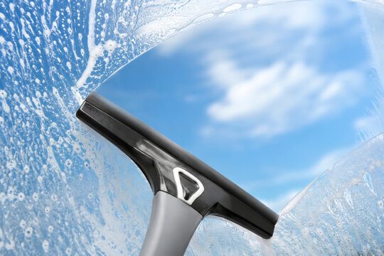 Squeegee cleaning dirty window glass with soap foam. Process of window cleaning for residential and commercial maintenance. Professional housework and hygiene service concept.