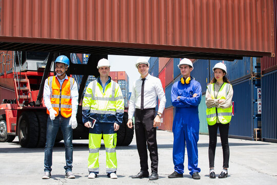 Diverse team collaborates within busy container yard utilizing shipping containers and forklift equipment; professionals wearing white helmets and work attire convey teamwork during logistics operatio