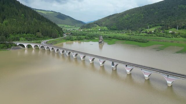 Aerial perspective of the Poiana Largului viaduct crossing the muddy waters of Lake Izvorul Muntelui, surrounded by green hills in Romania