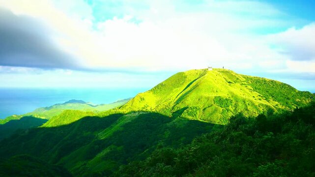 Green rolling hills meet ocean under bright blue sky with clouds.
