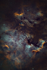 Fototapeta premium A cosmic nebula fills the frame, presenting swirling clouds of teal, orange, and dark dust against a starry background.