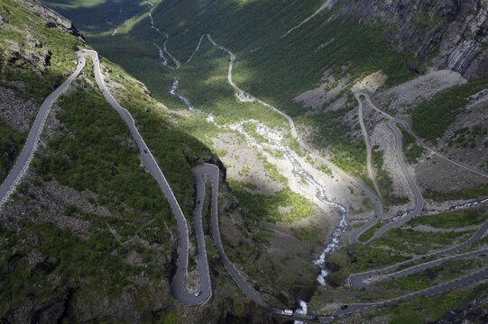 A winding road meanders through a green valley between steep mountains, Trollstigen, Andalsnes, Norway