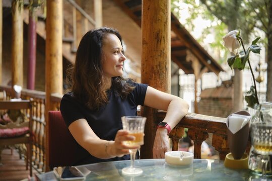 Cheerful and relaxed woman drinking white wine at rustic outdoor cafe enjoying tranquil ambiance of cozy cafe