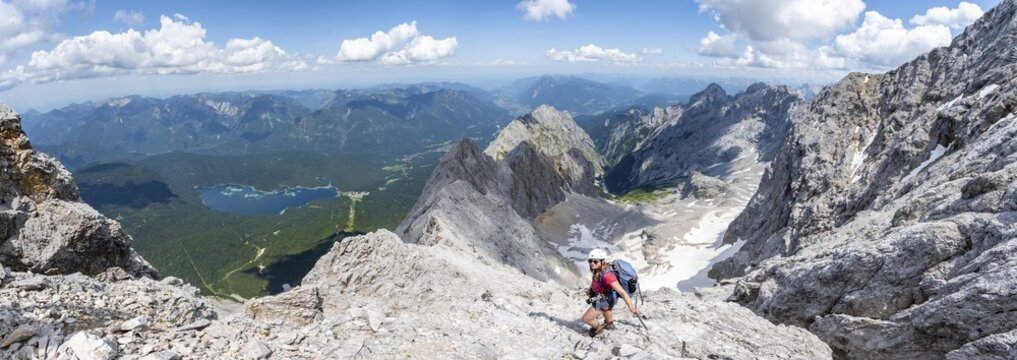 Panorama, mountaineer with helmet in a secured via ferrata, Zugspitze via ferrata, ascent to the Zugspitze, view of Eibsee lake and mountain basin with snowfield of the H&ouml;llentalferner and H&ouml;llental, Wetterstein range, Wetterstein range, Bavaria, Germany