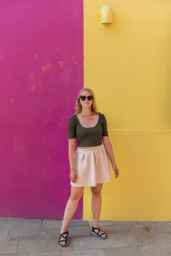 Young woman in dress stands laughing in front of colorful house, yellow and pink house facade, Burano Island, Venice, Veneto, Italy