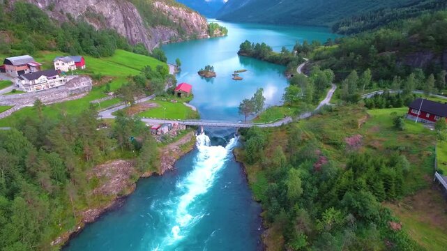 Aerial drone footage showing turquoise glacial river flowing through scenic norwegian mountains landscape with wooden cabins.