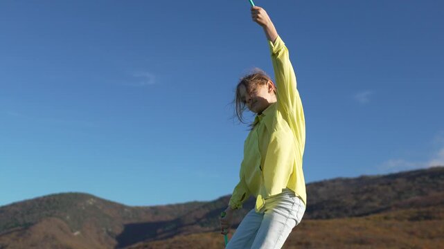 Gymnastics clubs athlete juggling maces outdoors in sunny mountain landscape against clear blue sky