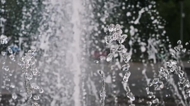 Clear water droplets splash and dance in extreme slow motion against a blurred outdoor park background. Concept of purity, fresh summer cooling, liquid physics, and abstract hygiene.