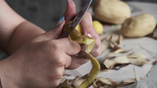 A close-up view of female hands carefully removing skin from a raw potato using a small knife. Concept of domestic lifestyle, preparing fresh organic ingredients, and traditional cooking.