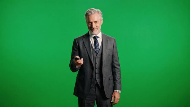 Confident mature businessman using presentation remote clicker. Senior corporate executive in suit looking at camera on green screen. Professional speaker and business leadership chroma key portrait