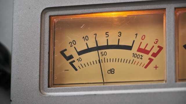 A close-up view of an analog VU meter needle fluctuating to measure audio levels on vintage equipment. Concept of music production, nostalgic technology, and high fidelity sound recording.