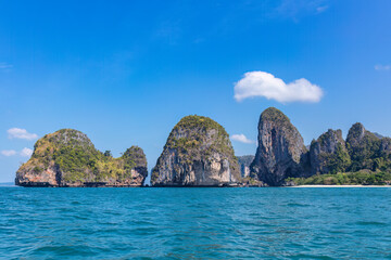 Naklejka premium Limestone sea stack islands near the shore of Railay Beach, in Krabi, southern Thailand. Blue Andaman Sea, cloudy blue sky. 