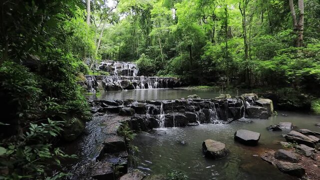 The video background features a natural landscape of a waterfall in a large forest. Sam Lan Waterfall in Saraburi National Park has beautiful flowing water.