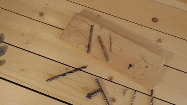 Metal drill bits and screws are neatly arranged on a light pine plank atop a wooden workbench.