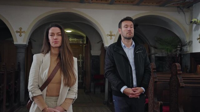 Couple walking quietly and reverently through a church, bowing toward the altar, entering a pew, and taking seats for prayer.