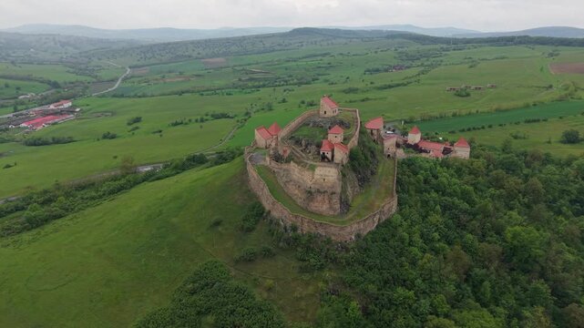 Stunning aerial view of the historic Rupea Citadel, a medieval fortress in Transylvania. The camera orbits the ancient stone walls on a green hill