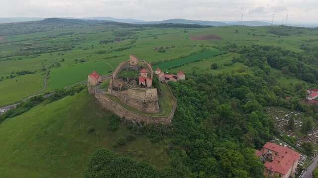 Aerial view circling the historic Rupea Fortress, a medieval landmark sitting on a hill overlooking the town and green landscape of Transylvania