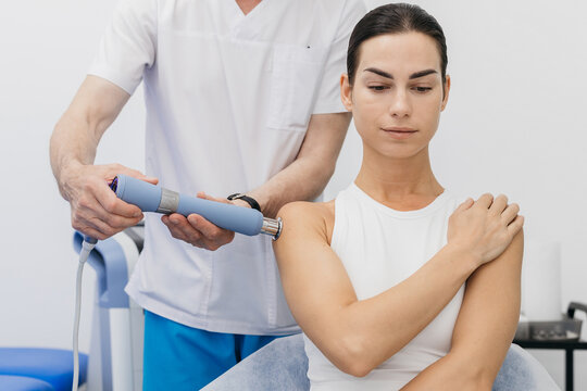 Doctor administering shockwave therapy to a female patient in a clinical setting, focusing on shoulder treatment with specialized medical equipment
