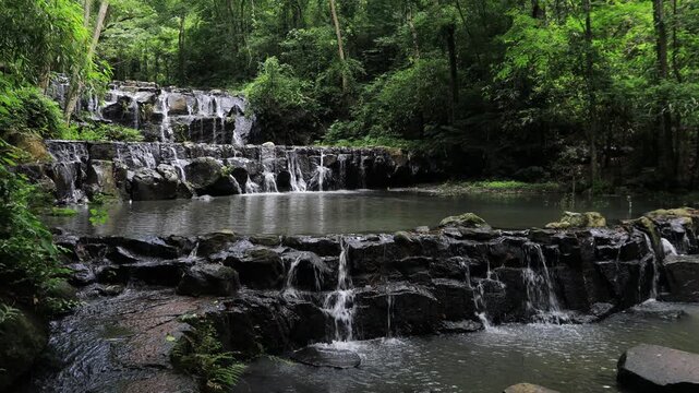 The video background features a natural landscape of a waterfall in a large forest. Sam Lan Waterfall in Saraburi National Park has beautiful flowing water.