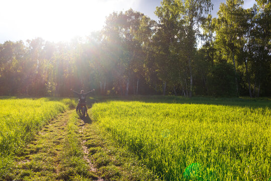 Cyclist with arms wide open riding a bike on a rustic dirt path through a grassy meadow, surrounded by a swarm of gnats in the warm glow of a beautiful golden hour summer sunset