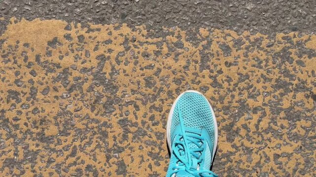 A person wearing a blue sneakers stepping on a crosswalk with yellow and white stripes while crossing the street. Close-up