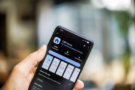 Close-up of a hand holding a smartphone displaying the CBP Home app interface on Google Play Store
