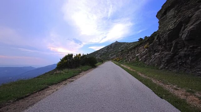 Mountain road winding beside rocky slope beneath dramatic cloud sky