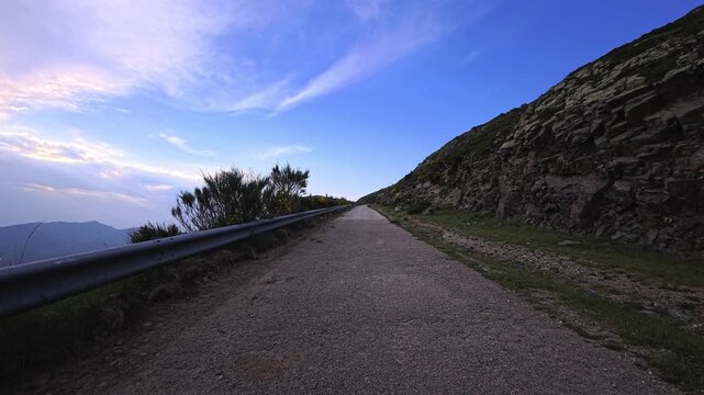 Mountain road with guardrail beside rocky hillside under evening sky