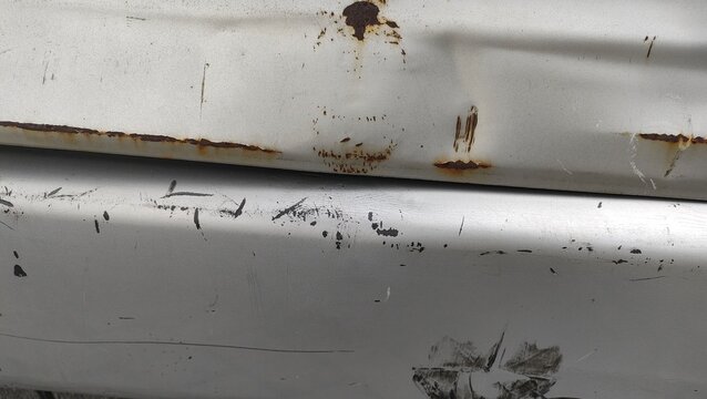 Close-up of a damaged, dented, and rusted white car body panel. Concept of vehicle accident, automotive damage, auto body repair, and insurance claim.