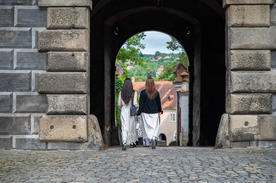 Zwei Frauen in wei&szlig;en Kleidern gehen durch ein historisches Schlosstor 