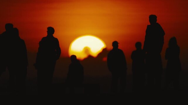 Group of silhouetted individuals standing against a vibrant sunset, showcasing the gradual transition of light and shadow in an outdoor setting